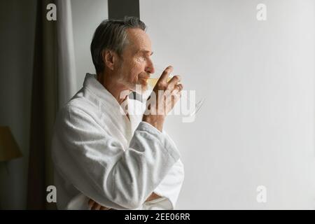 Side view of an elderly man drinking wine while looking at window Stock Photo