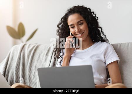 Smiling woman freelancer talking on phone and using laptop Stock Photo