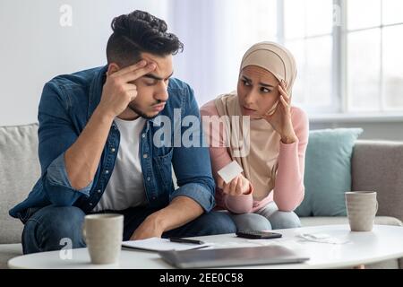 Confusded lady in hijab showing bill her upset husband Stock Photo