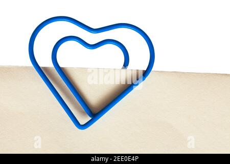 blue heart shaped paperclip paper clip on white cream coloured paper - keep together, stay together concept Stock Photo