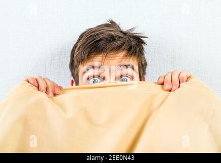 Frightened Young Man under Blanket in the Bed at the Home Stock Photo