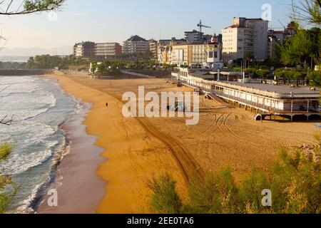 A digger beach cleaning on Sardinero beach Santander Cantabria Spain on a sunny spring morning with the Maremondo restaurant Stock Photo