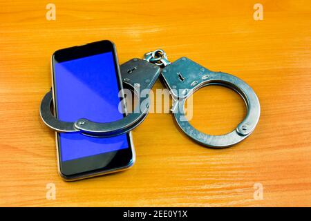 Handcuffs and Mobile Phone on the Wooden Table closeup Stock Photo