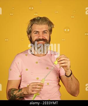 bearded man blowing soap bubbles. carefree man with bubble blower. happy hipster in playful mood. Fall into childhood. feeling childish and childlike. real happiness. april fools day. Stock Photo