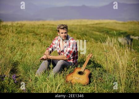 Guy with guitar contemplate nature. Inspiring nature. Pleasant time alone. Musician looking for inspiration. Dreamy wanderer. Wanderlust concept. Summer vacation highlands nature. Peaceful mood. Stock Photo