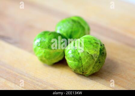 Group of three whole fresh brussels sprouts on wooden plate. Stock Photo