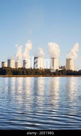 Power plant with smoking chimneys by a lake at sunset. Stock Photo
