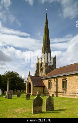 Exterior of historic St. Edith's Church (churchyard memorials, porch, tall spire & blue sky) - Bishop Wilton, East Riding of Yorkshire, England, UK. Stock Photo