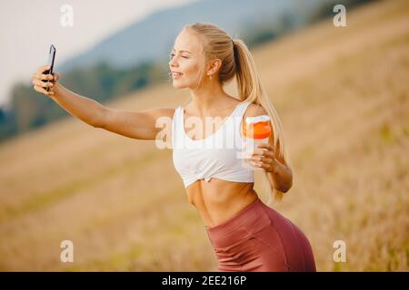 Beautiful blonde woman makes selfie photo on phone during sports training, smiling camera. Stock Photo