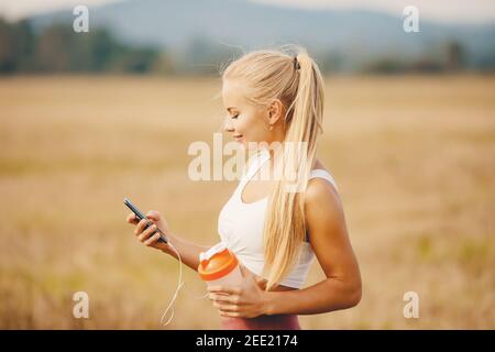 Beautiful blonde girl chooses music playlist for running in park. Stock Photo