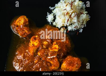 Chicken curry (in madras way), pieces of chicken meat in spicy sauce, rice with saffron on black background, closeup. Indian meal. Detail. Stock Photo