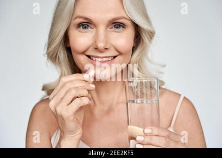 Smiling healthy middle aged 50s woman taking supplement vitamin pill. Stock Photo