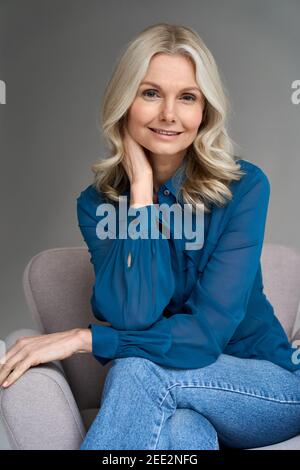 Smiling 50s middle aged woman model sitting in chair looking at camera. Stock Photo