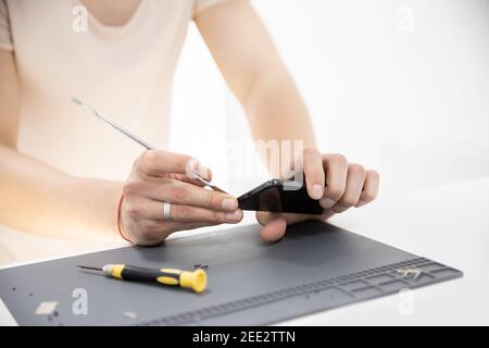 Master disassembles modern mobile phone, repairs and replaces battery, broken screen. Stock Photo