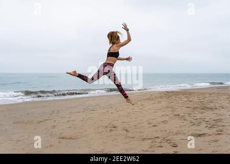 Fitness athletic woman jumping on the beach during working out exercises.Concept of happiness, yoga and training lifestyle. Stock Photo