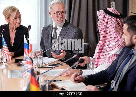 diverse delegates discussing points of their colleague speech, multi-ethnic meeting in modern boardroom, everyone in formal wear, sharing opinions Stock Photo