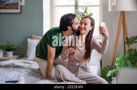 Young couple taking selfie in the morning on bed indoors at home. Stock Photo