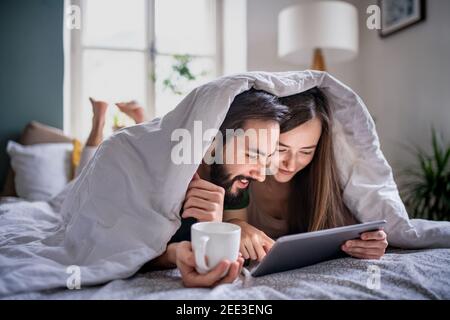 Young couple in love using tablet on bed indoors at home. Stock Photo