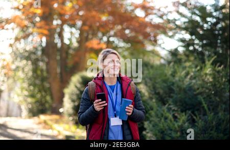 Woman caregiver, nurse or healthcare worker outdoors on the way to work, using smartphone. Stock Photo