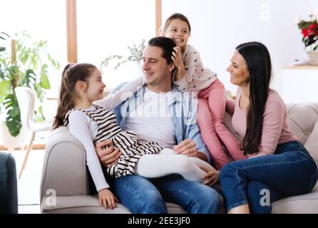 Parents with small daughters sitting on sofa indoors at home, relaxing. Stock Photo