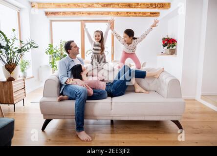 Parents with small daughters sitting on sofa indoors at home, relaxing. Stock Photo