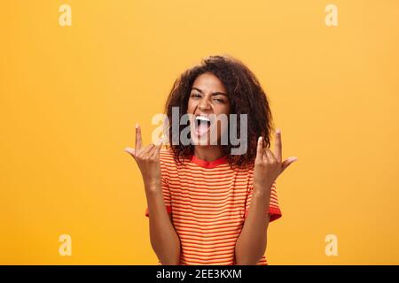 Waist-up shot of amazed happy stylish african american woman feeling awesome rocking on party yelling from joy and satisfaction showing rock n roll Stock Photo