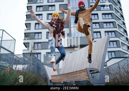 Cheerful young couple owners jumping outdoors in front of new flat, new home and relocation concept. Stock Photo