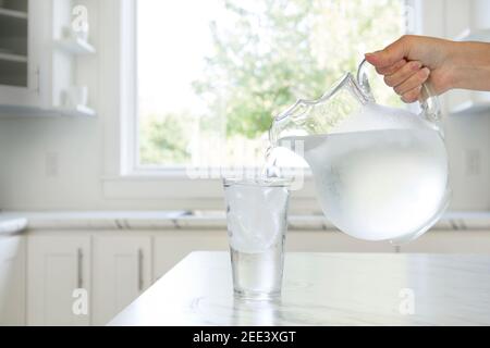 A woman’s hand pouring ice water from a pitcher into a glass. Stock Photo