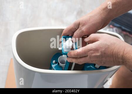 A plumber installs a water pump in a ceramic toilet cistern. Drainage system installation, home repair. Stock Photo