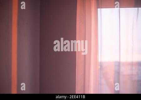 the rays of the morning sun on the wall in an empty room fall through the white tulle on the window. New day, atmospheric mood. Stock Photo