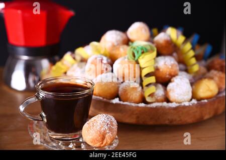 Espresso coffee is poured from a geyser coffee maker. Baked castagnole with powdered sugar. Traditional sweet pastries in hand. Street food, round biscuits with sugar for the carnival of Venice.  Stock Photo