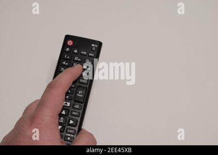 Hand holding black multimedia tv remote control on yellow background.Pushing button to change tv channel. Stock Photo