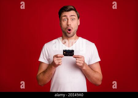 Photo of shocked person open mouth staring hands hold debit card isolated on dark red color background Stock Photo