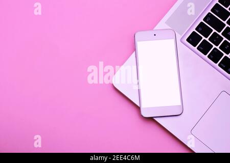 Mockup image of white mobile phone with blank white screen with Modern pink office desk with laptop for input the text on copy space Top view, flat la Stock Photo
