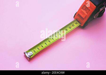 An old metal measuring tape on pink background. Copy space, selective focus. Stock Photo