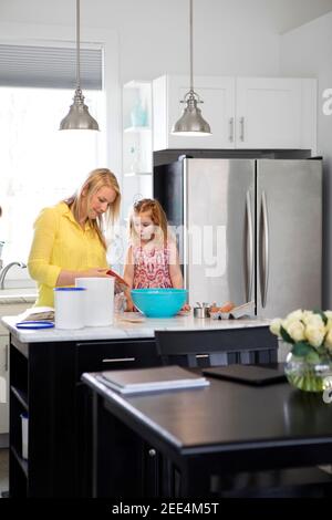 A mom and her toddler daughter baking together in a modern kitchen. Stock Photo