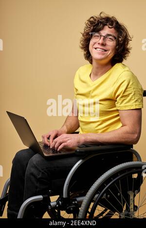 man disabled student preparing for exam using laptop, sitting on wheelchair isolated in studio. portrait. online education for handicapped people Stock Photo
