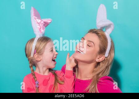 Happy mother and child daughter celebrating Easter. Cute little girl with funny face in bunny ears laughing, smiling and having fun. Stock Photo