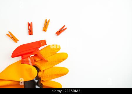 Black cleansing spray in hand in orange glove and multicolored clothespins on white background. Cleaning, cleanliness and household chemicals concept. Stock Photo