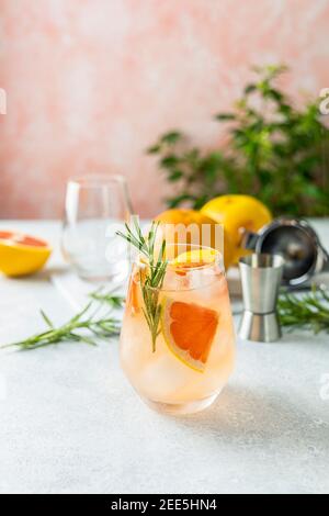 Tequila cocktail with grapefruit juice, tinted with the aroma of a fresh sprig of rosemary on fashion pastel pink background.