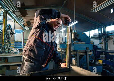 The handyman measuring the metal bar he's working in the workshop on work surface. Stock Photo