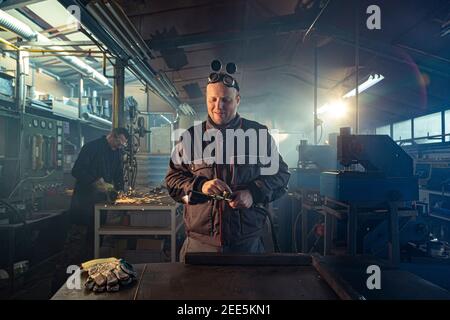 Handyman preparing his autogenous welding tool for work while his colleague can be noticed in the back working on his grinding task. Stock Photo