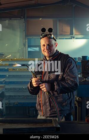 Handyman preparing his autogenous welding tool for work while his colleague can be noticed in the back working on his grinding task. Stock Photo