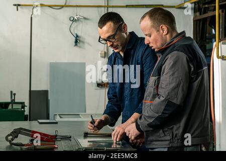 A tinsmith and his fellow colleague engineer are working together on a work task in their workshop. Stock Photo