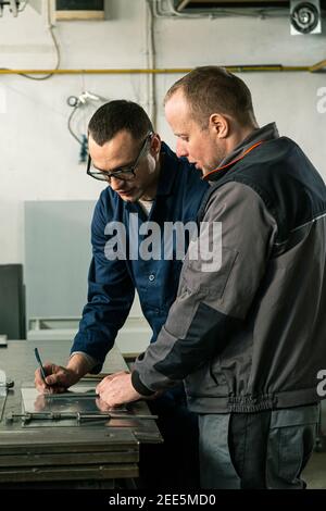A tinsmith and his fellow colleague engineer are working together on a work task in their workshop. Stock Photo