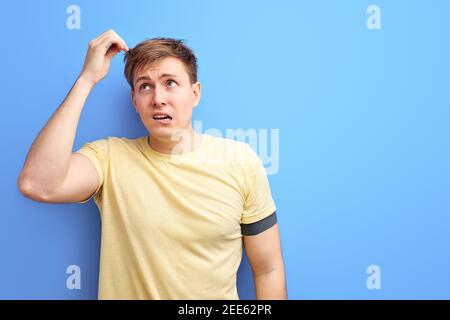 man looks away and thinks with a doubtful face, try to remember something, isolated on blue background. studio portrait of caucasian male in casual t- Stock Photo