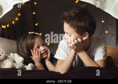 Siblings lie in a hut of chairs and blankets. Brother and sister smiling, playing at home Stock Photo