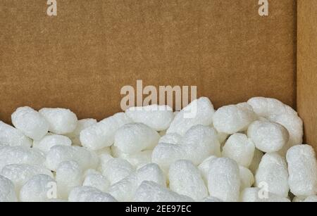 White packing peanuts styrofoam popcorn packaging material inside a cardboard box, angle view with copy space. Stock Photo