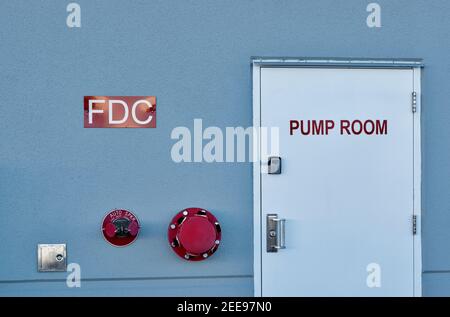 Fire pump room door with signs and wall fixtures on an industrial warehouse exterior. Stock Photo