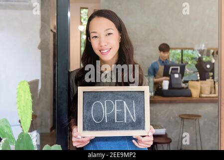 Young Asian woman entrepreneur showing open sign at front door of her coffee shop Stock Photo
